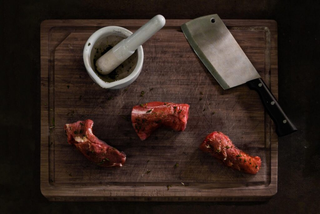 photo looking down at cutting board with cleaver, mortar and pestle, and three pieces of sliced meat